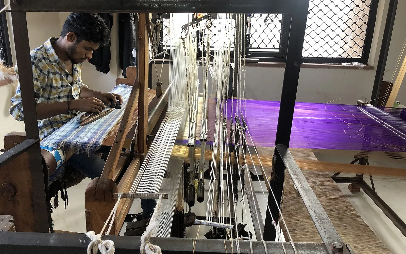 A weaver working at a handloom with fine white warp threads, weaving a Chanderi saree