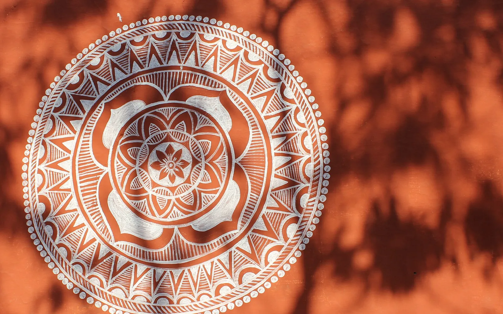 A circular white mandana design painted on a red earth wall