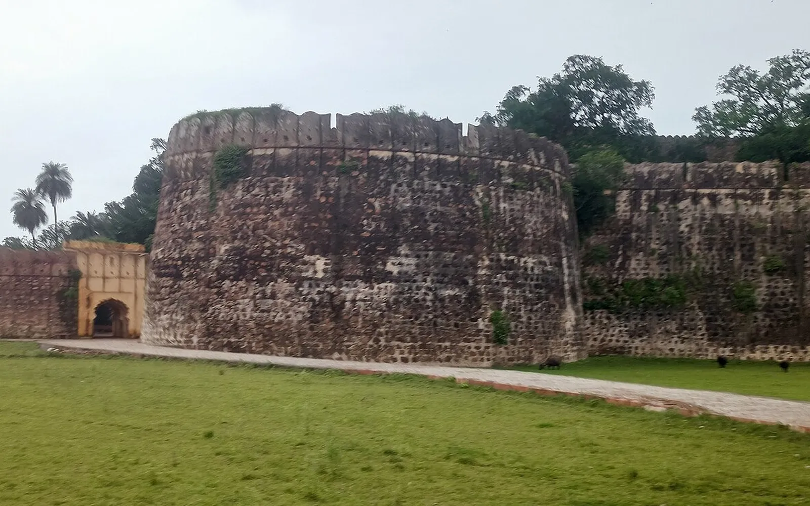 Round stone bastion and curtain walls of Shergarh fort in Baran district beside a green lawn